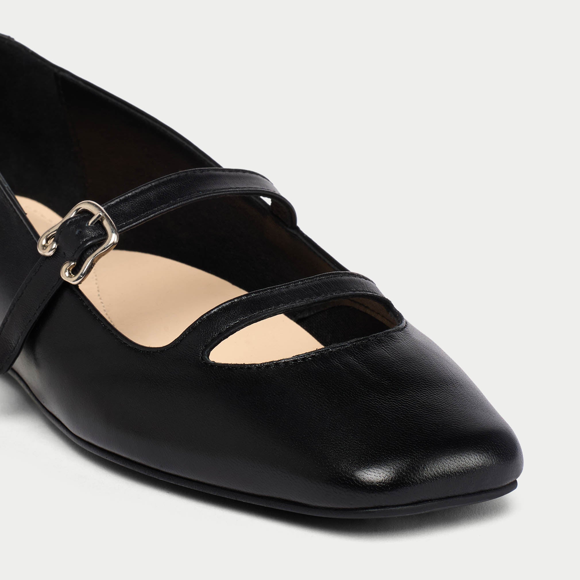 Black leather flat shoe with a strap on a light gray background