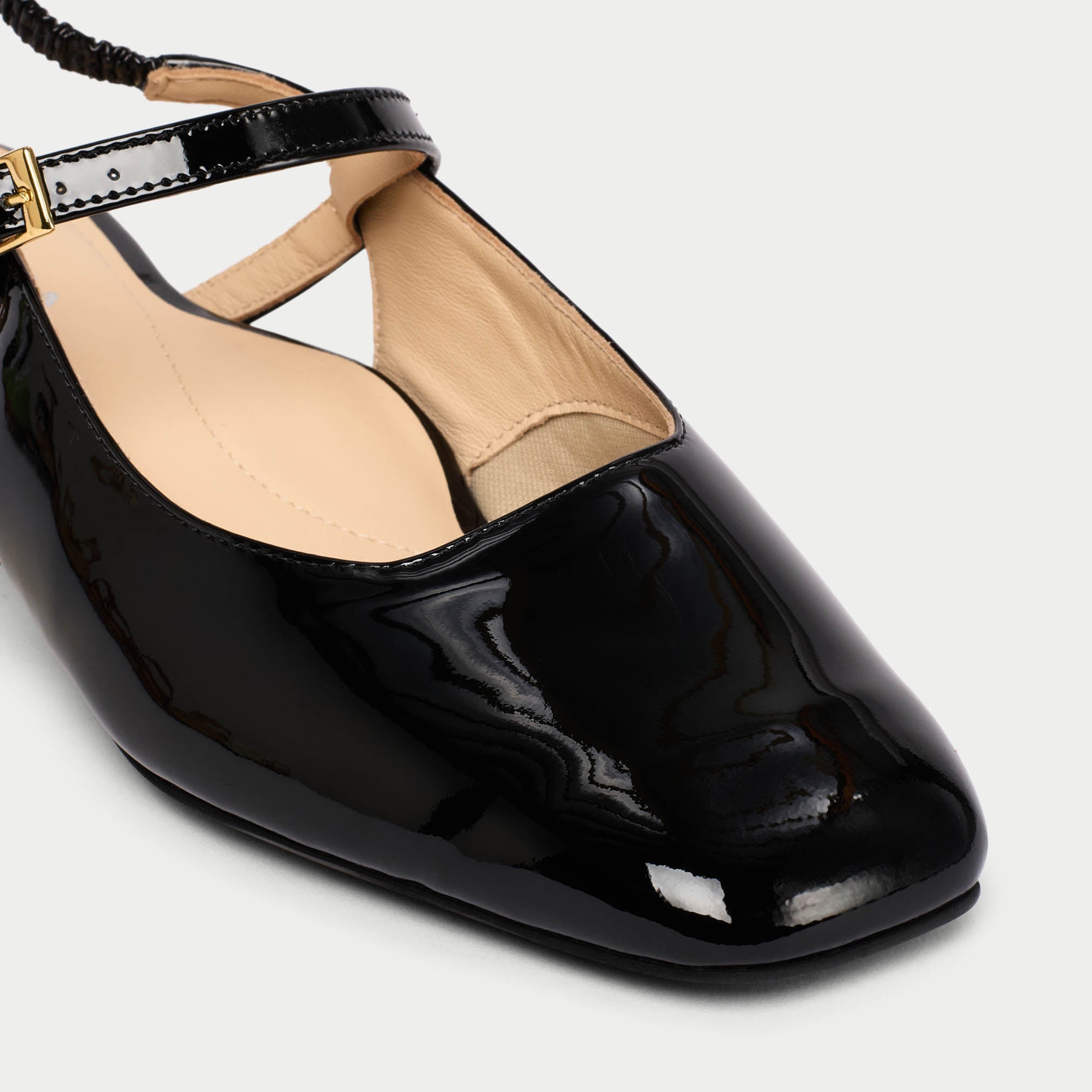 Black patent leather flat shoe with a gold buckle on a light gray background