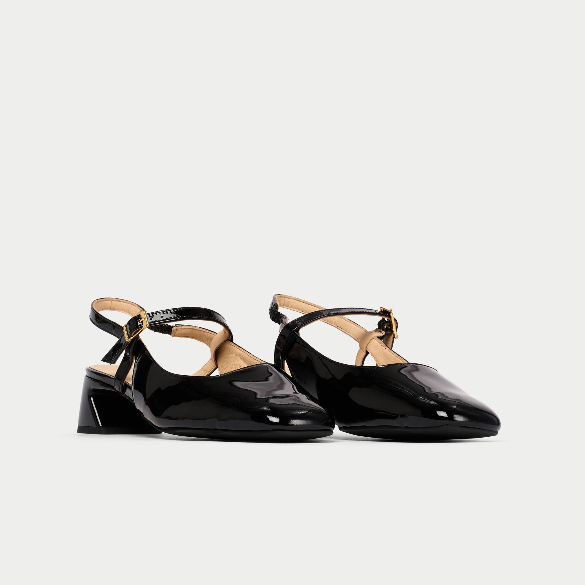 Black patent leather shoes with thin straps on a light gray background