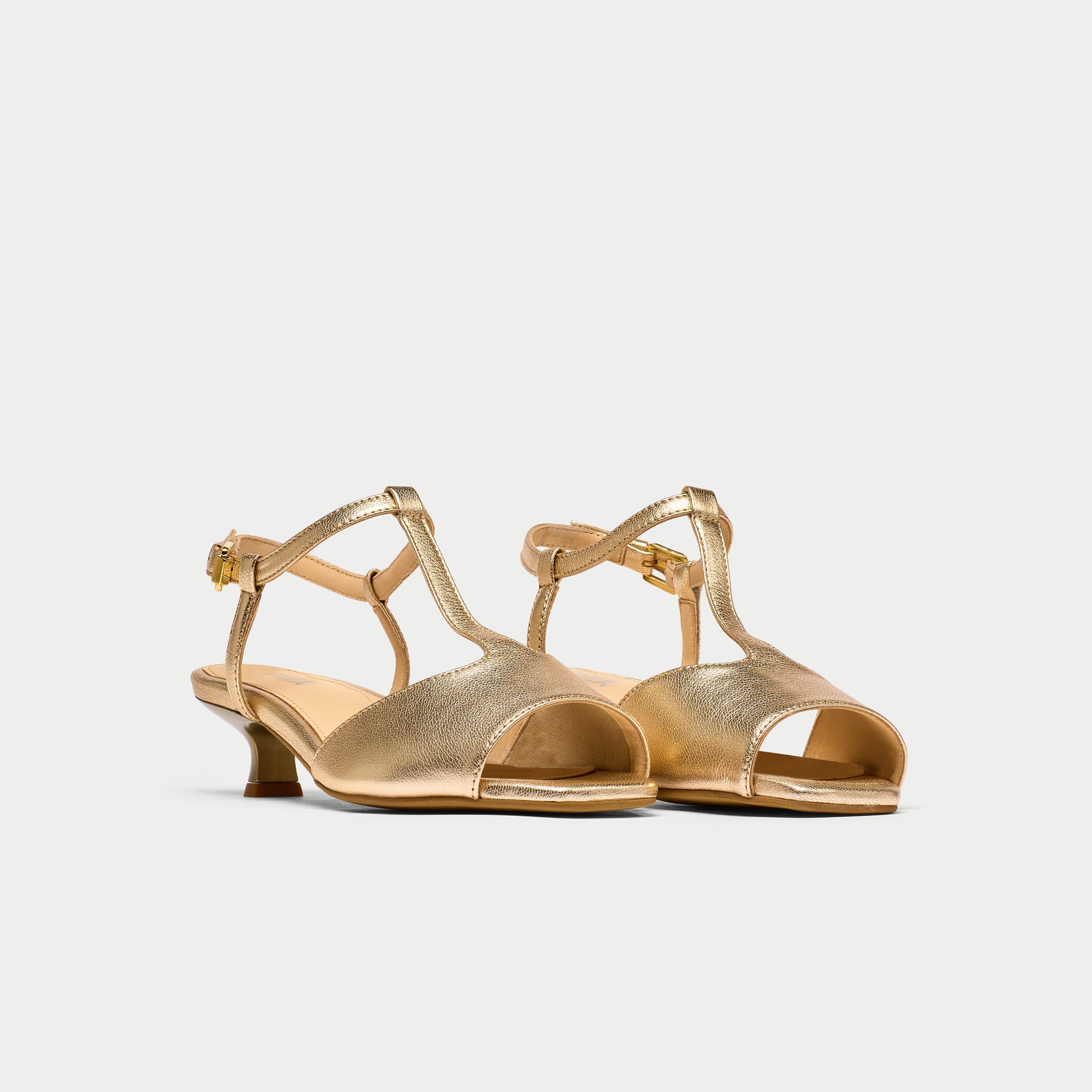 Pair of gold open-toe shoes with thin straps on a light gray background
