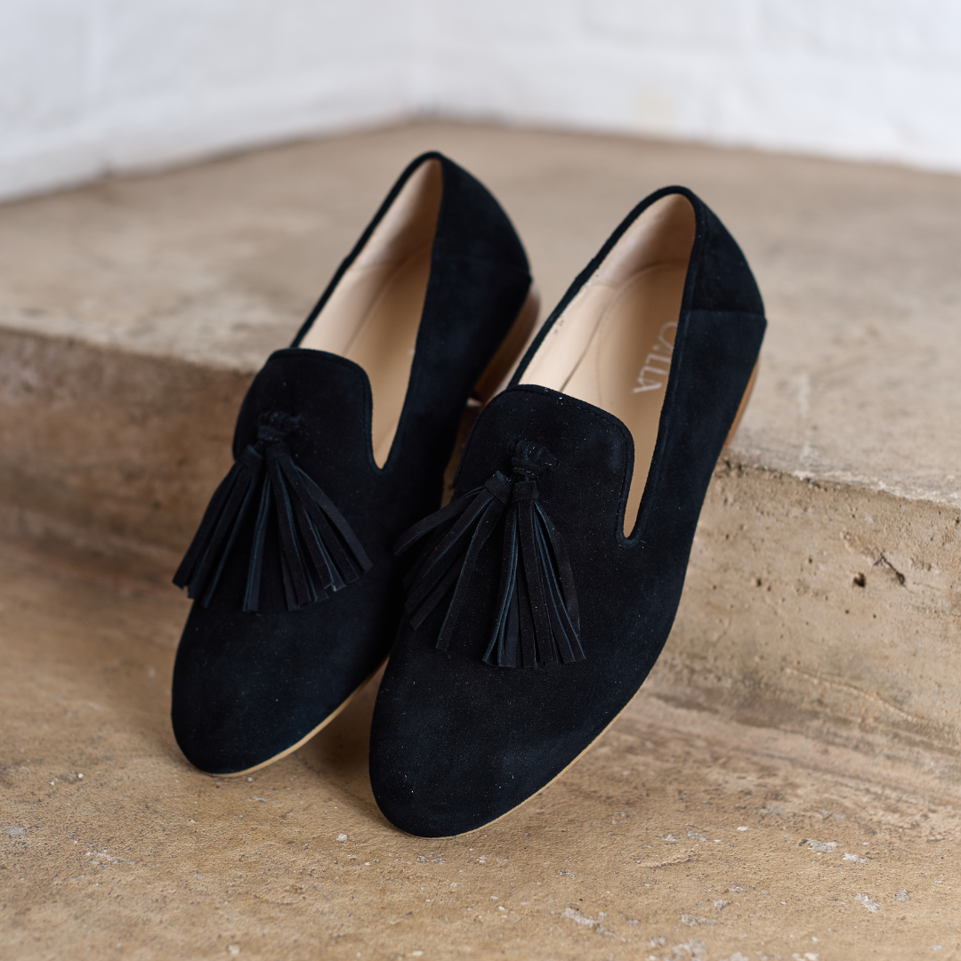 Pair of black loafers with tassels on a textured surface
