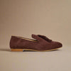 Brown suede loafer with tassel on a light beige background