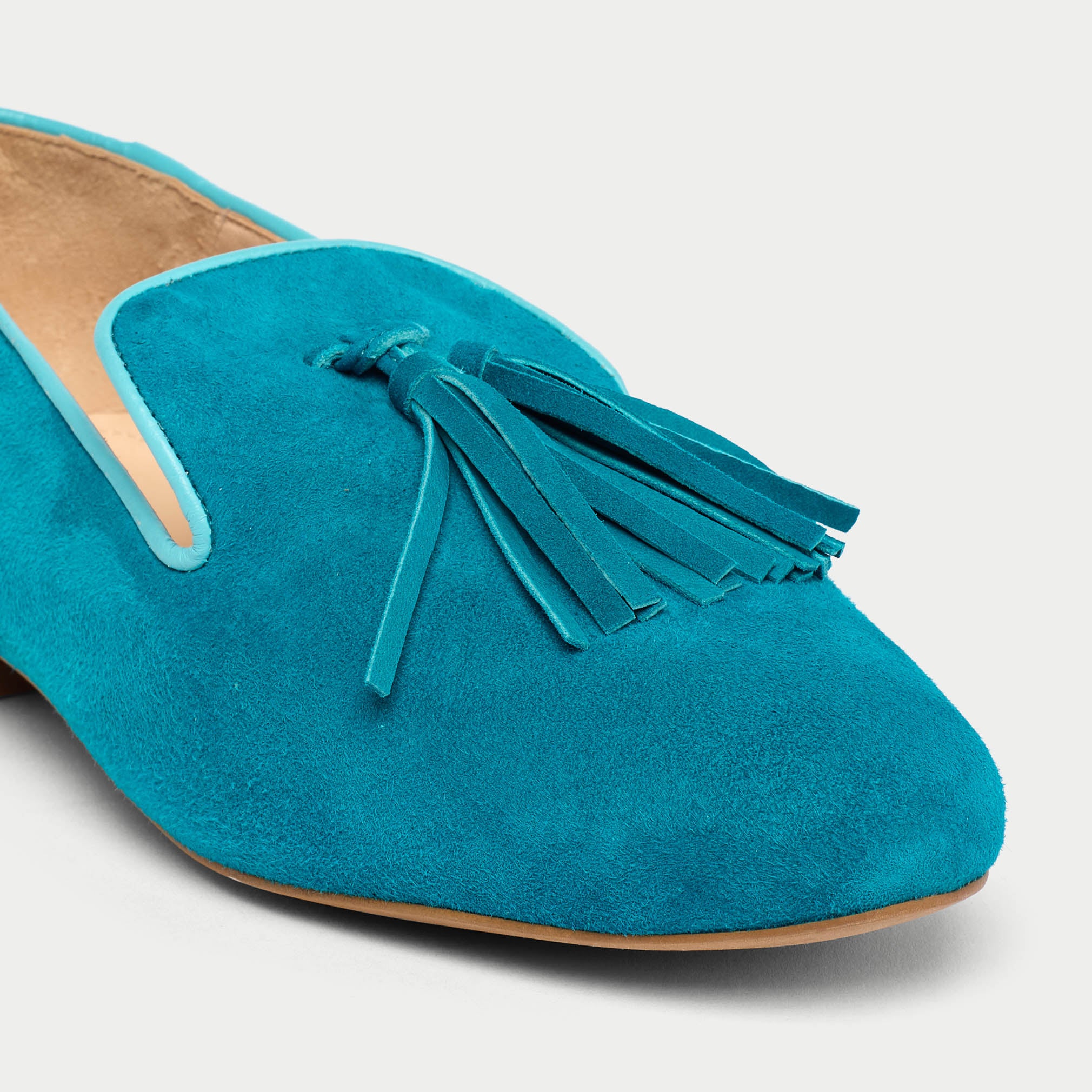 Blue suede loafer with tassel on a light gray background