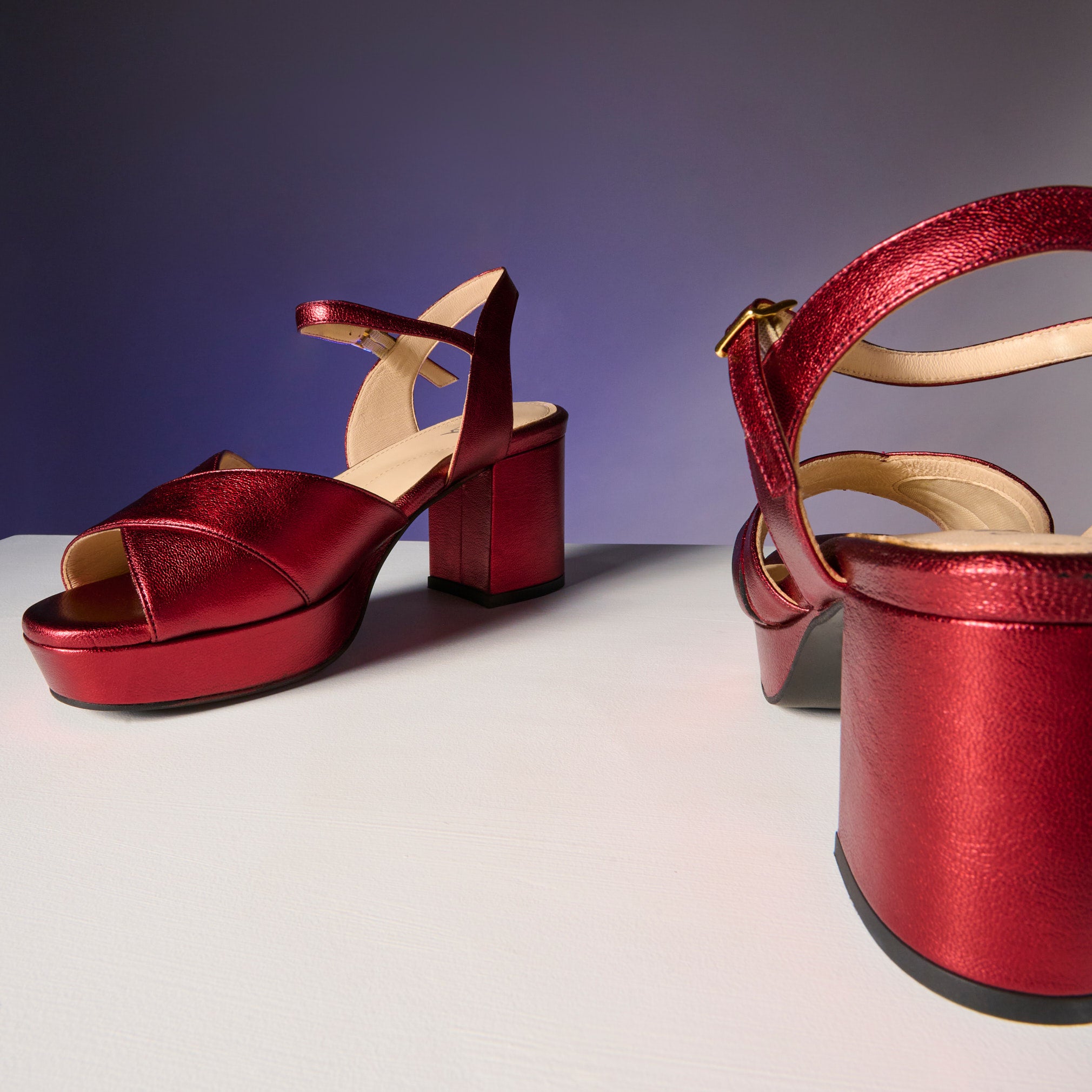 Red high-heeled shoes on a white platform with a purple gradient background