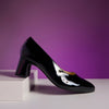 Black patent leather shoe on a white platform with a purple background