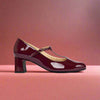Maroon patent leather shoe with a strap on a light red background