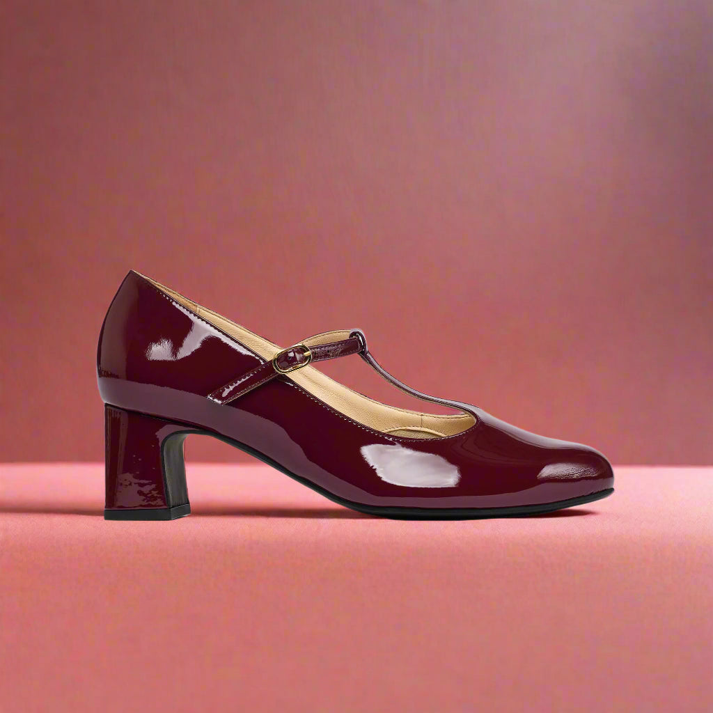 Maroon patent leather shoe with a strap on a light red background