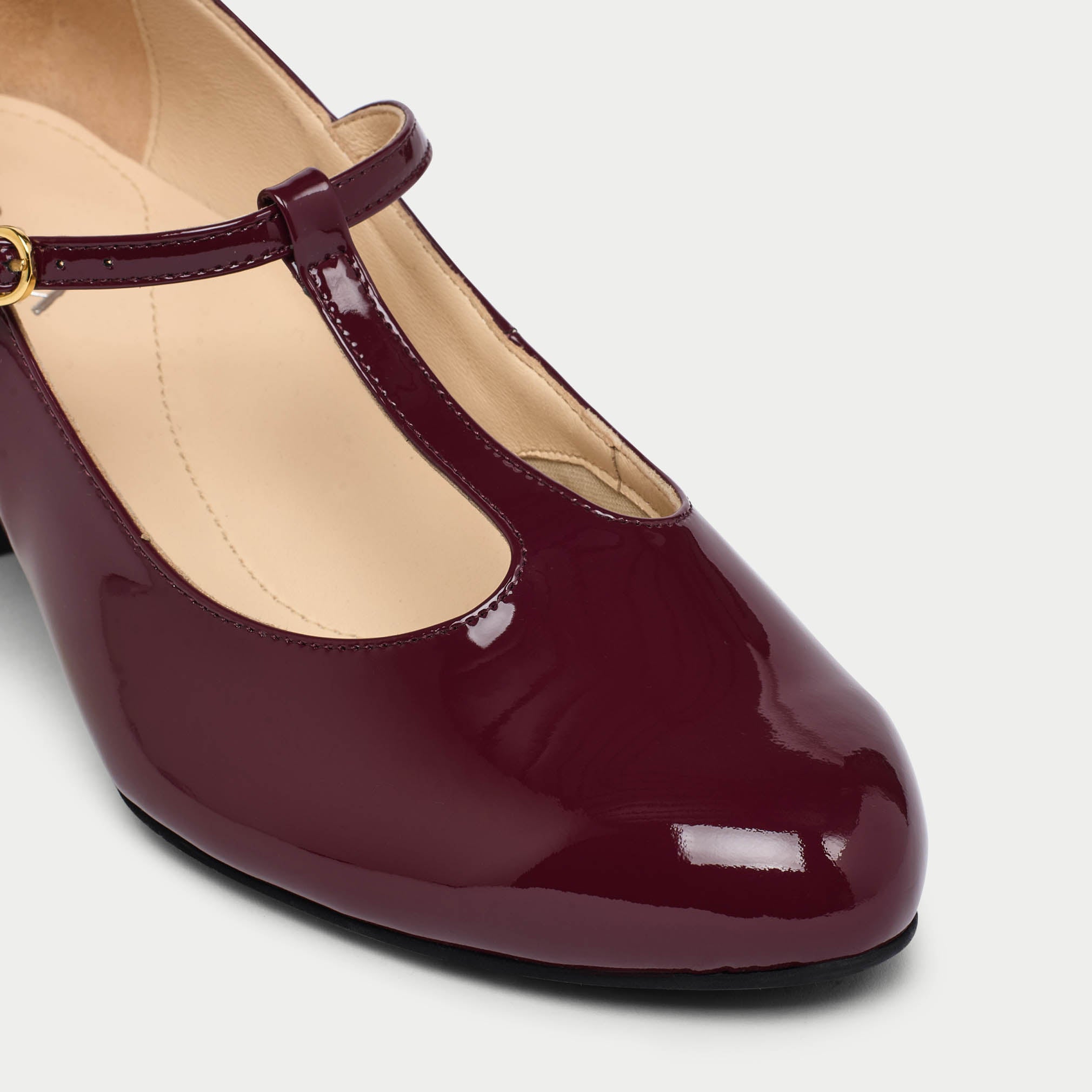 Maroon patent leather high heel shoe on a light gray background