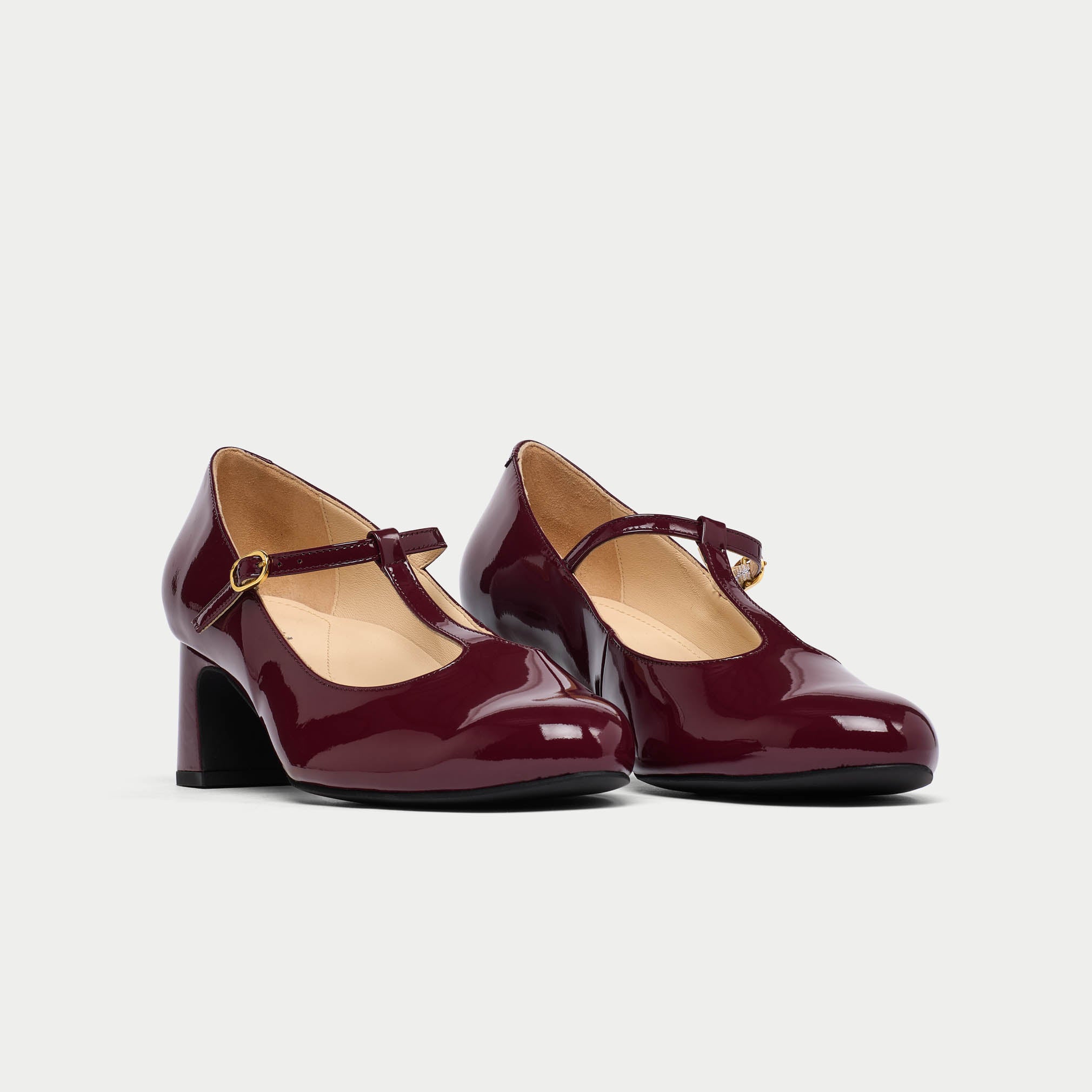 Pair of burgundy high-heeled shoes with a strap on a light gray background