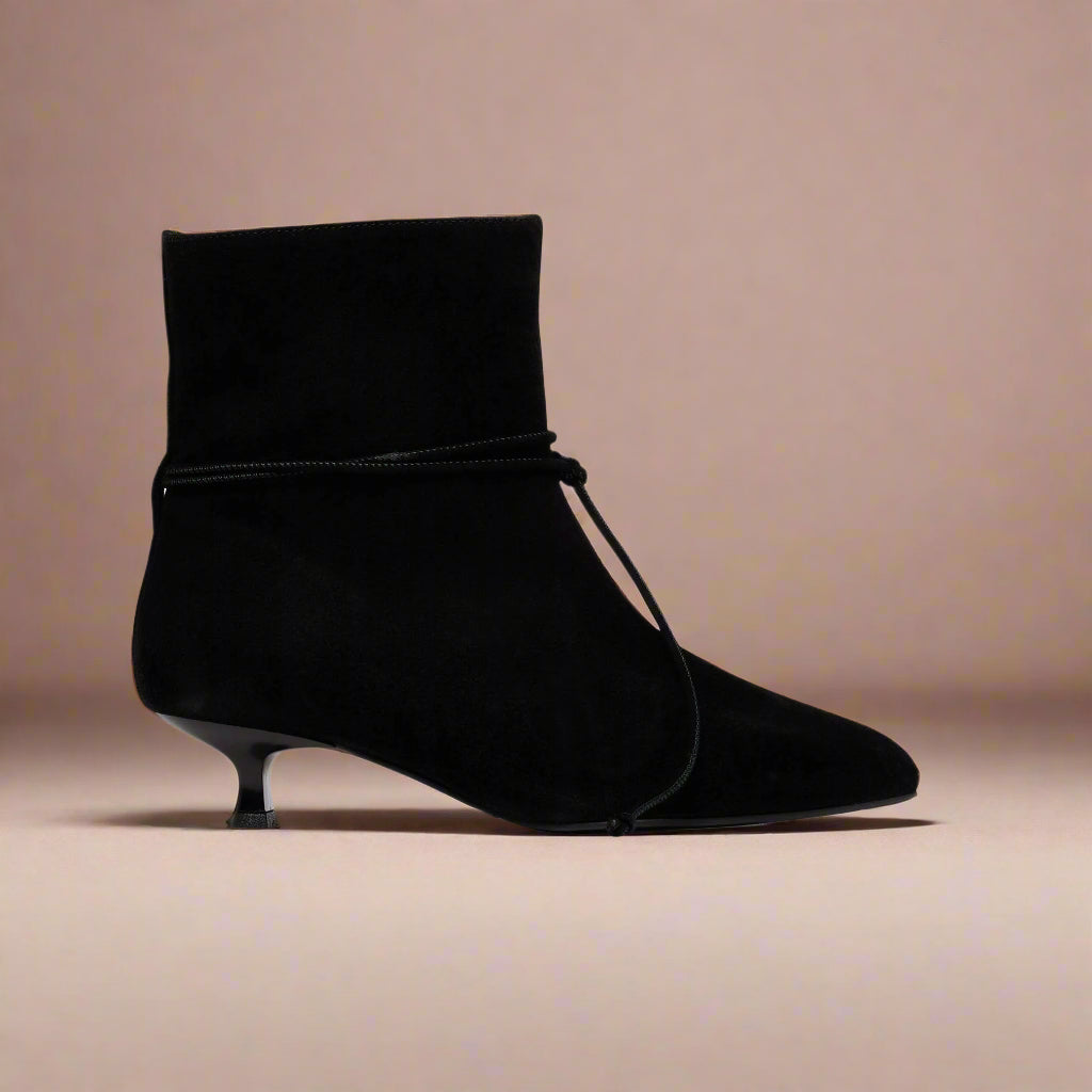 Black ankle boot with a kitten heel on a light pink background