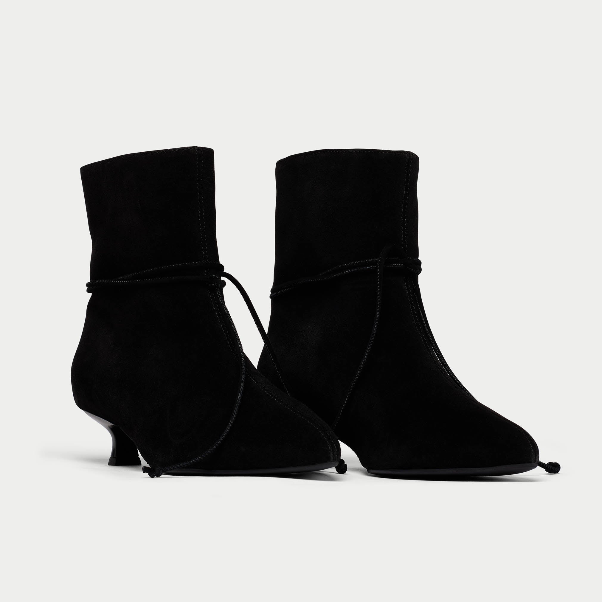 Pair of black suede ankle boots on a light gray background