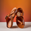 Brown leather sandals with gold buckles on a white surface and orange background
