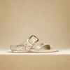 Silver sandal with a gold buckle on a beige background