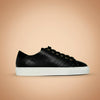 Black leather sneaker with white sole on a beige background