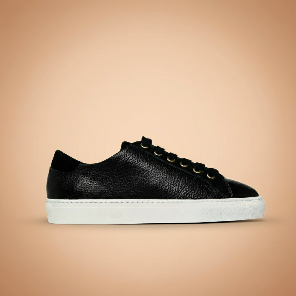 Black leather sneaker with white sole on a beige background