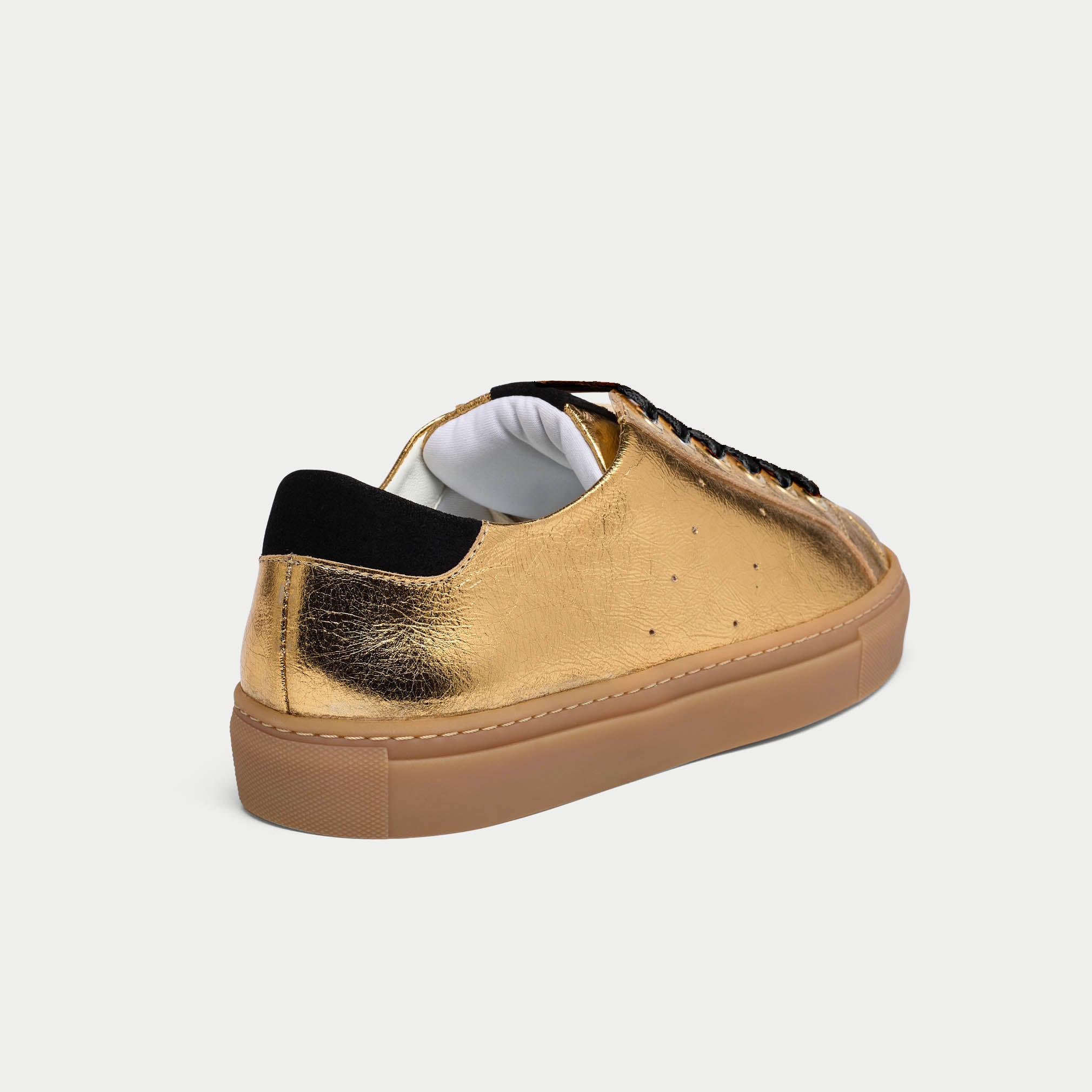 Gold sneaker with black sole on a light gray background