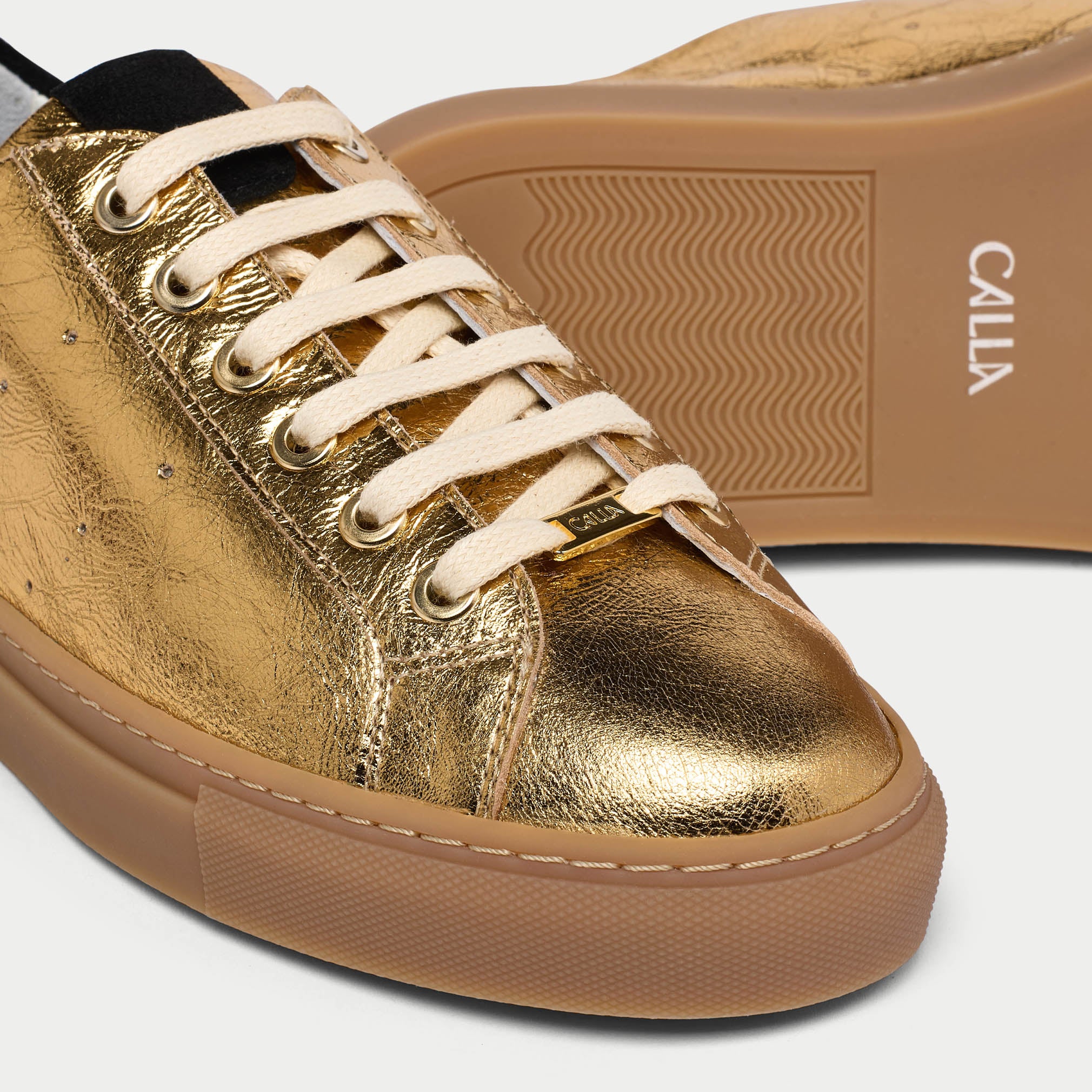 Gold sneaker with white laces and brown sole on a light gray background