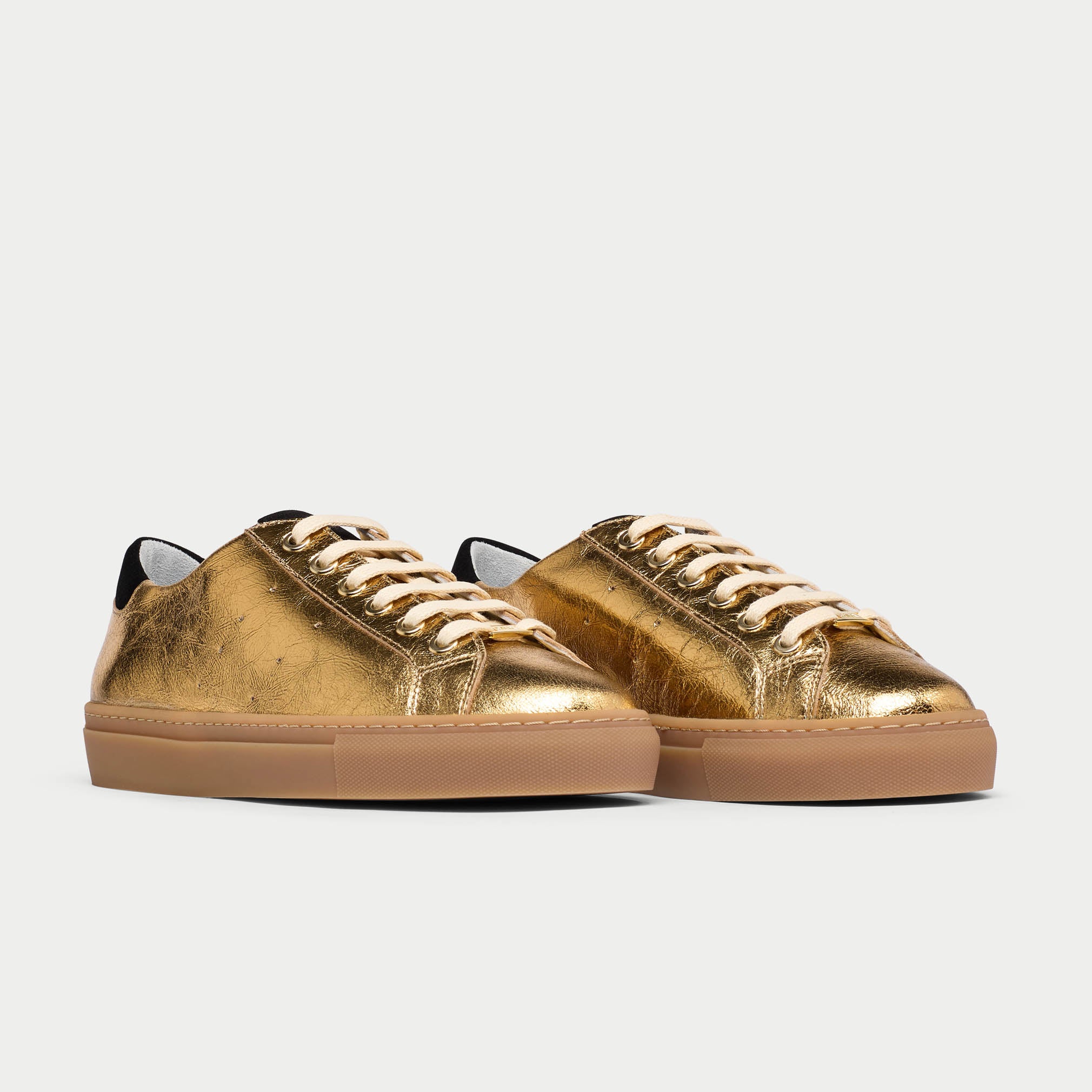 Gold sneakers with tan soles on a light gray background