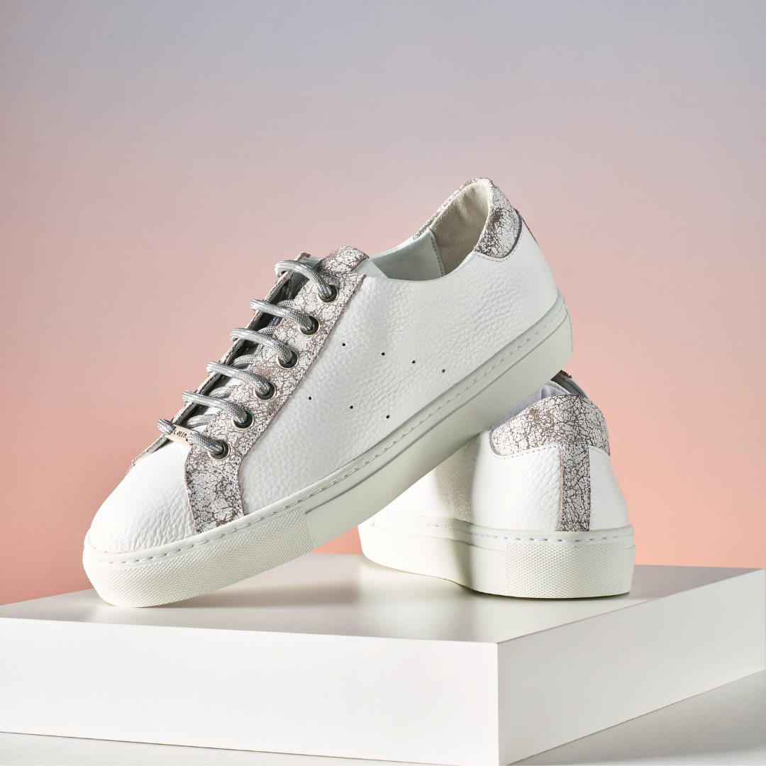 White sneakers with grey crackle on a white platform against a pink gradient background