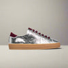 Silver sneaker with burgundy laces and sole on a light gray background