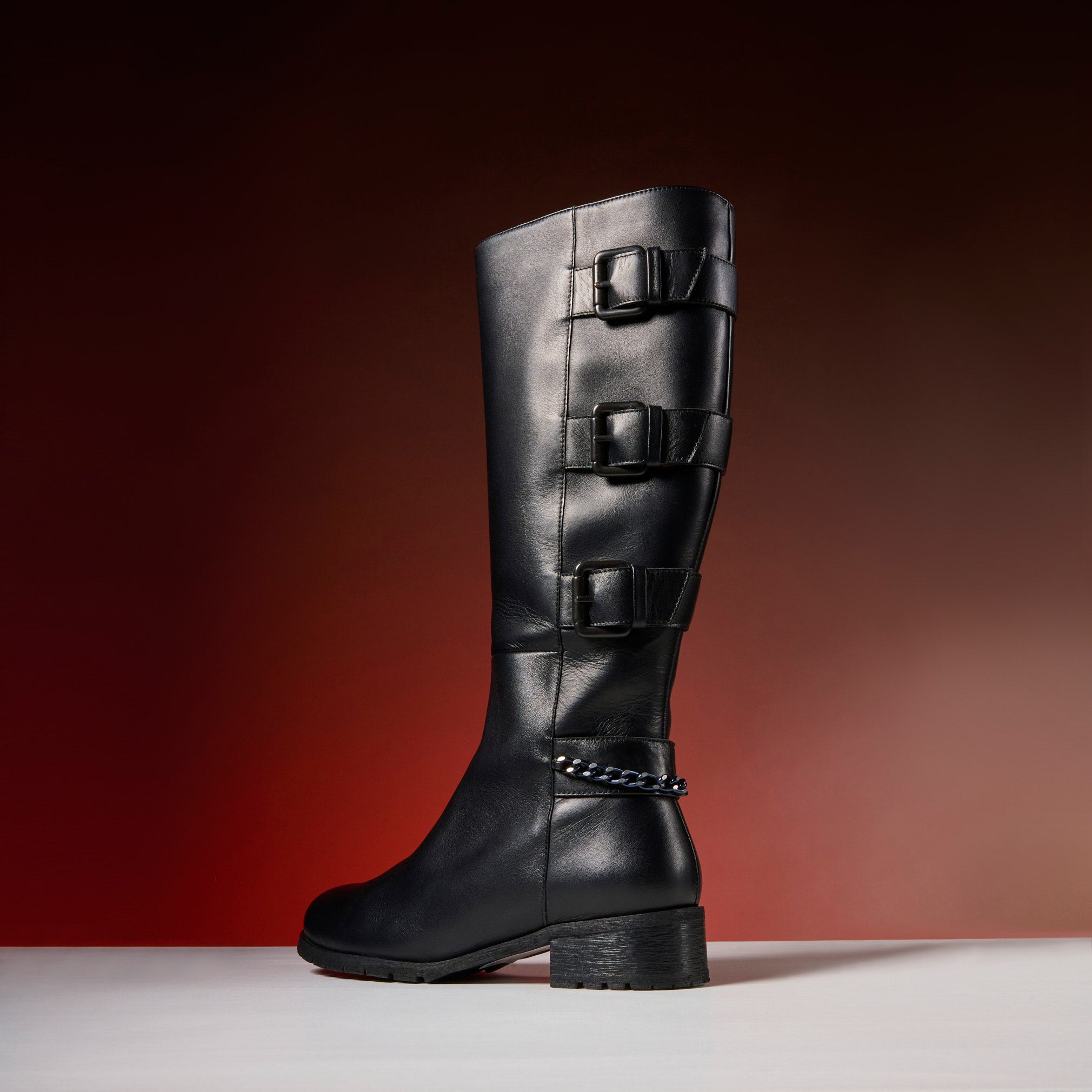 Black knee-high boot with multiple buckles on a gradient red background