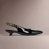 Black Thea patent leather slingback shoe with gold chain detail on a beige background