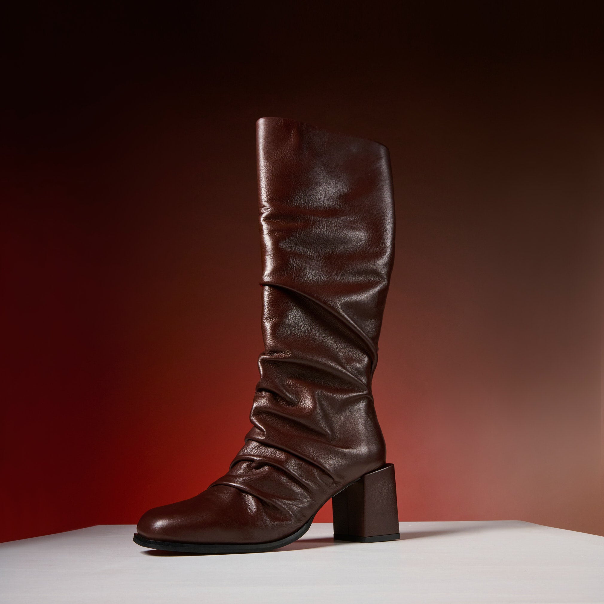 Brown knee-high boot on a white surface with a gradient red background