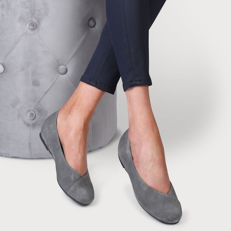 calla charlotte grey suede flat shoes for bunions as shown on a model who is sitting down on a grey chair