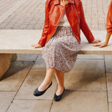 woman siting on bench in black shoes, leopard skirt and red jacket